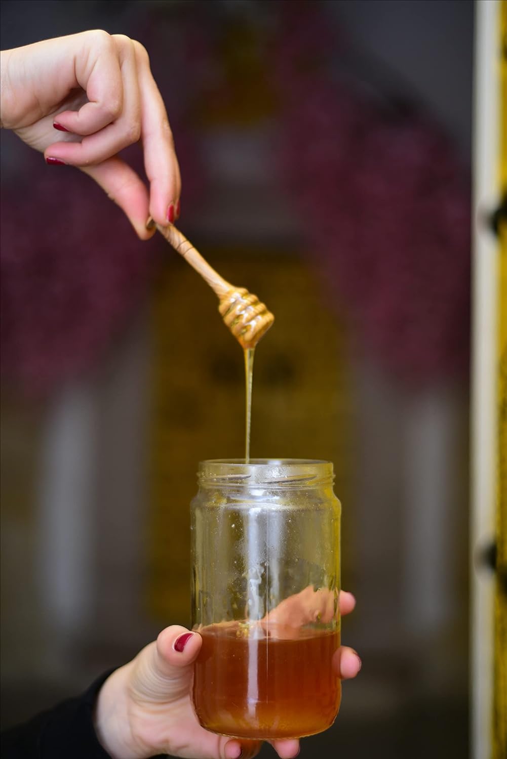 Honey drizzling from an olive wood dipper into a glass jar