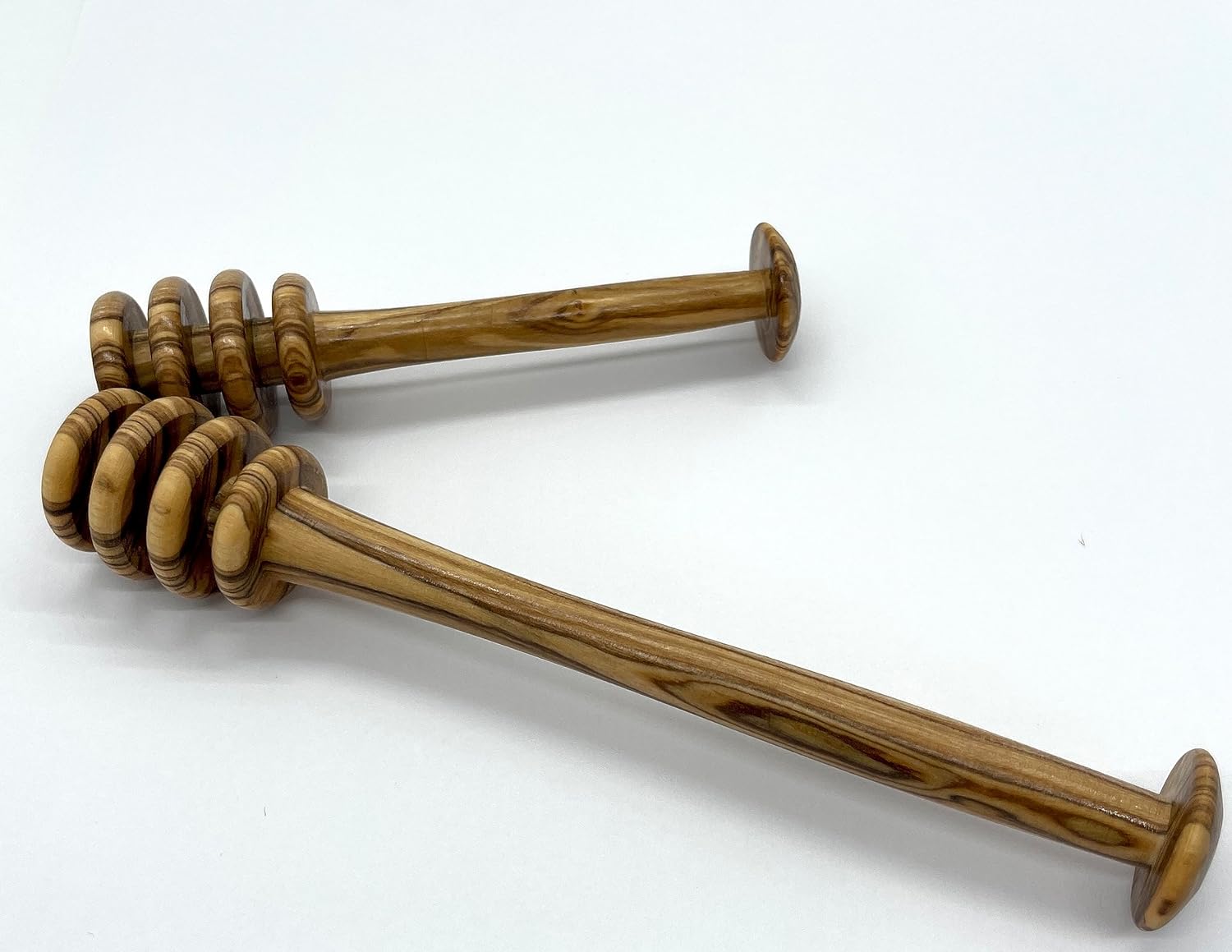 Two olive wood honey drizzlers laid on a white background